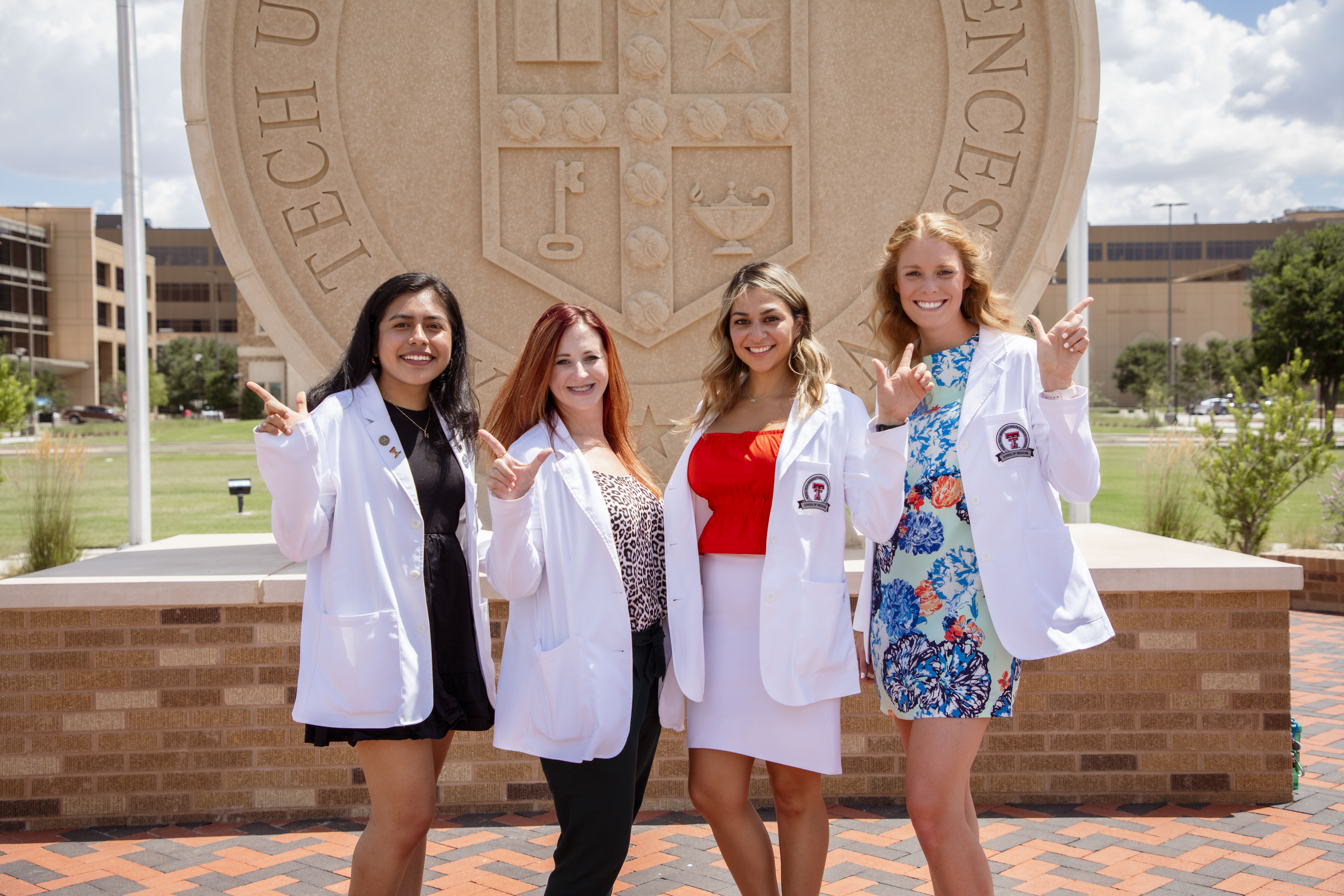 Four students smiling in front of University Seal